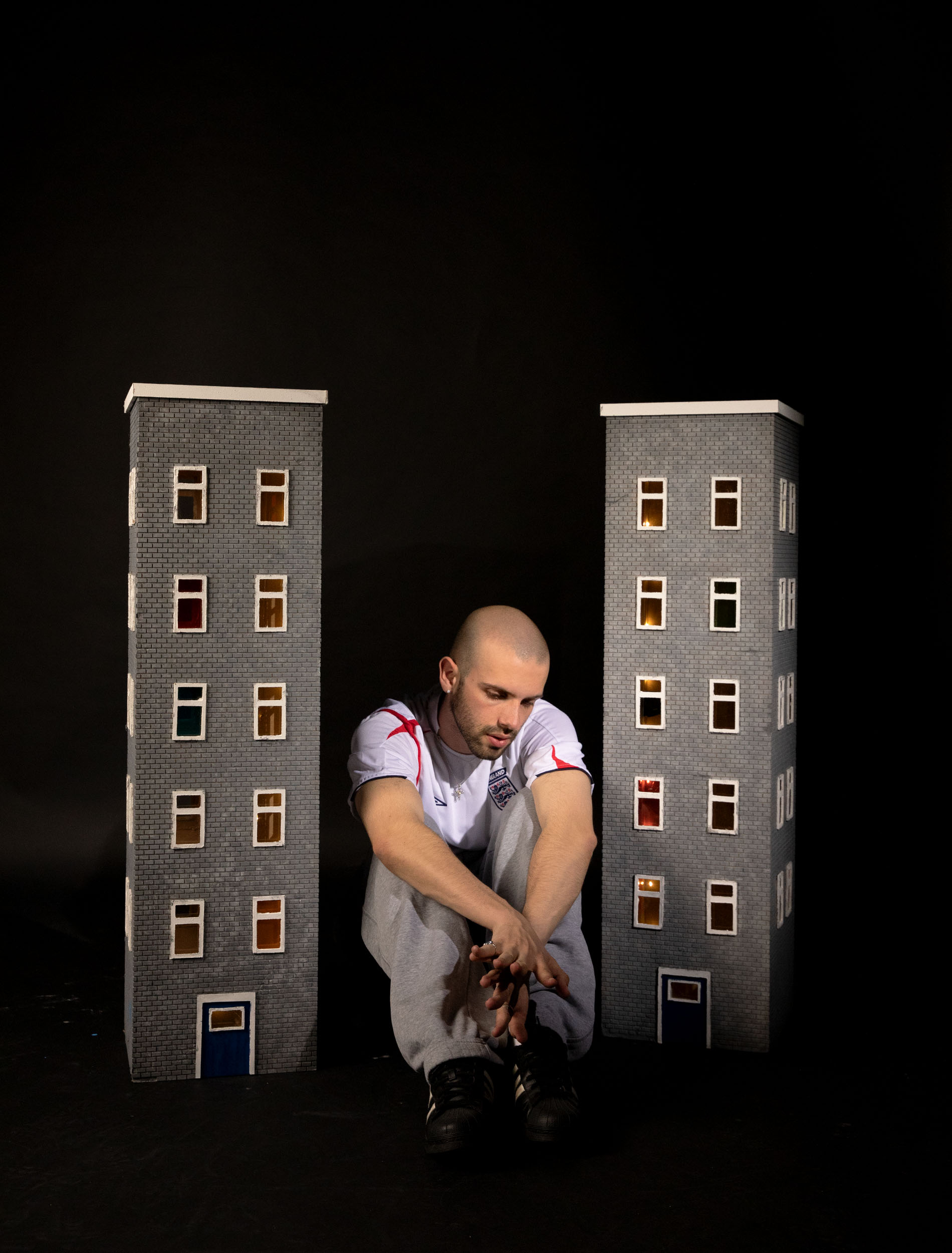Set Design and Art Directed by Annie Wicks showing an striking image of a man sitting between two model estate flat blocks.