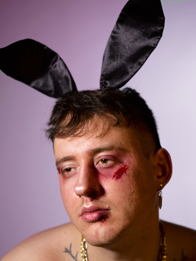 BA Hons photography shot by Charley Smith. SFX portrait shoot of a male model wearing black bunny ears. Visible tattoos and chains.