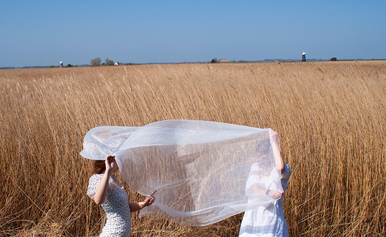 Fashion image photographed by Charlie Scurlock showing two models flying sheer fabric in a field and blue sky