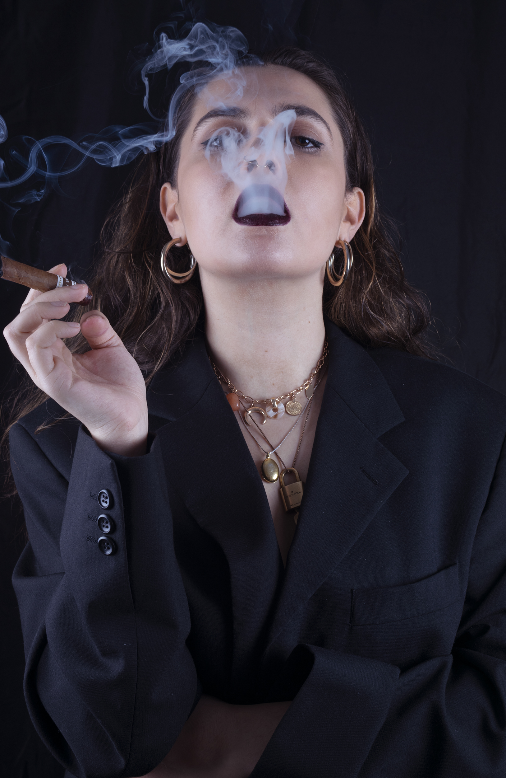 Black background, woman smoking in a suit, smoke surrounds her.