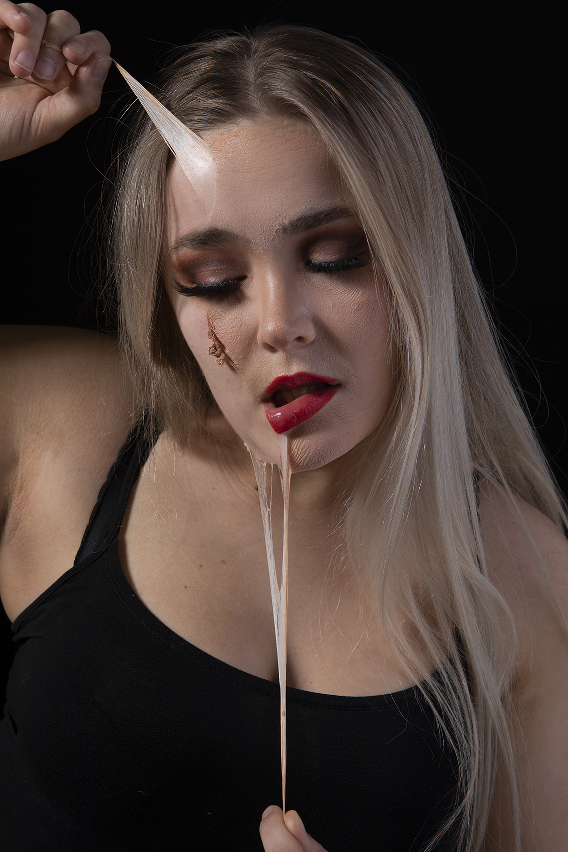 Black background, woman captured with liquid latex on her face pulling it off.