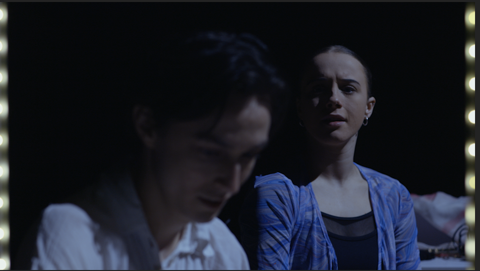Still from the film, Variation by Hannah Diver: The protagonist looks at himself in a mirror as his friend stands behind.