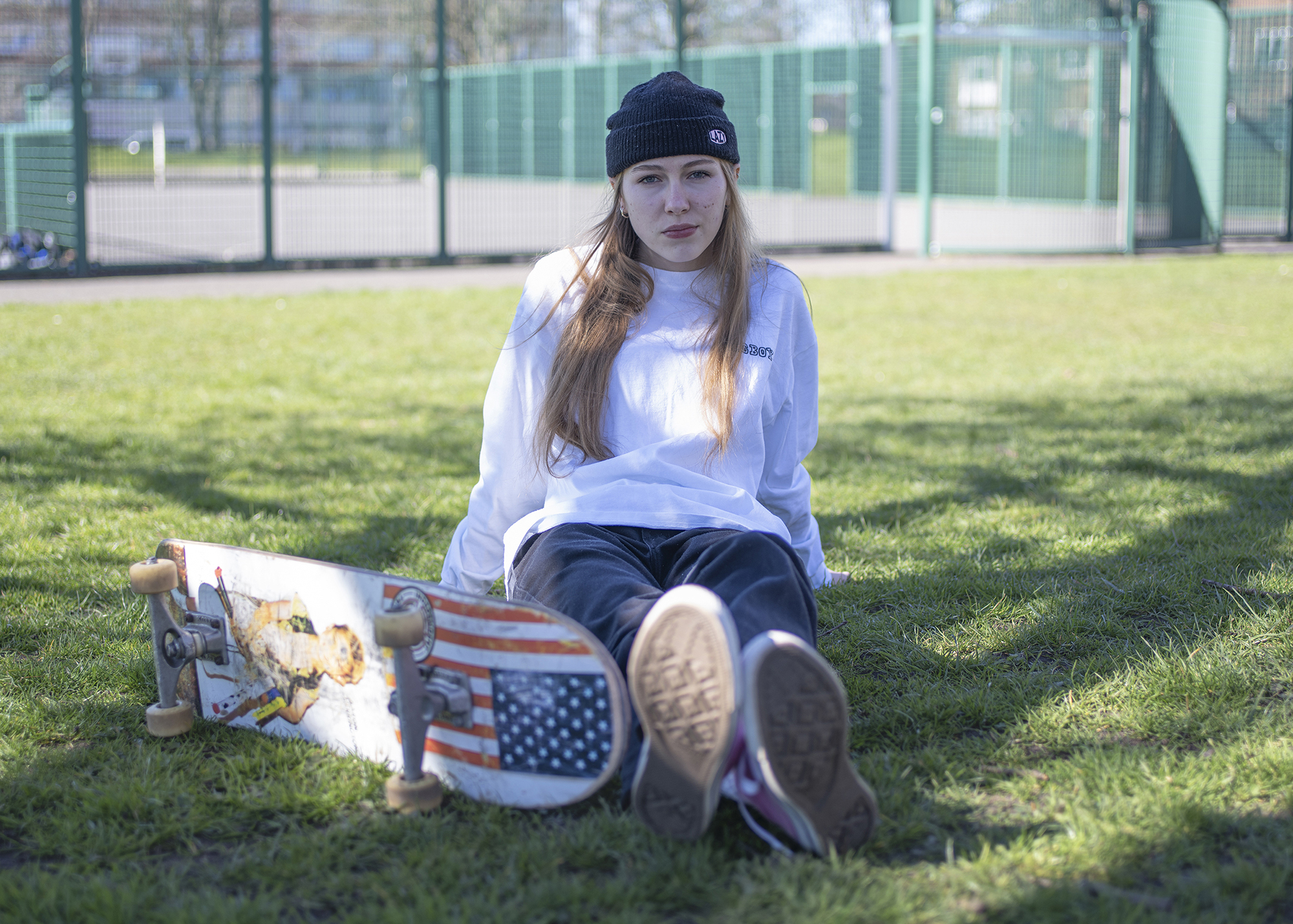 BA Photography work by Hannah Jayne showing a documentary style portrait of a skater girl sat in grass, legs outstretched next to her board.