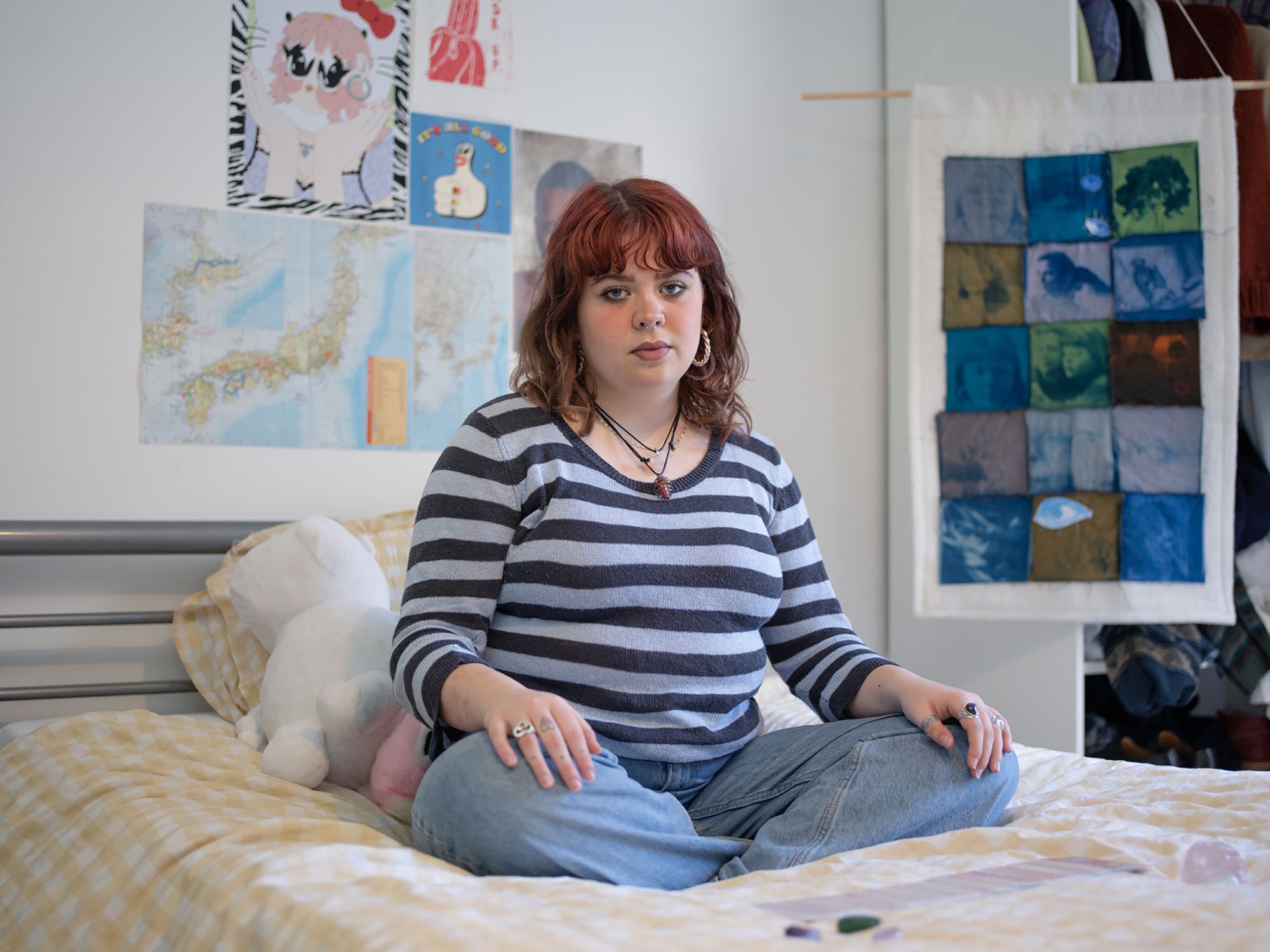 BA Photography work by Hannah Jayne showing a documentary style portrait of a woman sat on her bed, with tarot cards laid out in front of her, and a tapestry of her own making behind her.