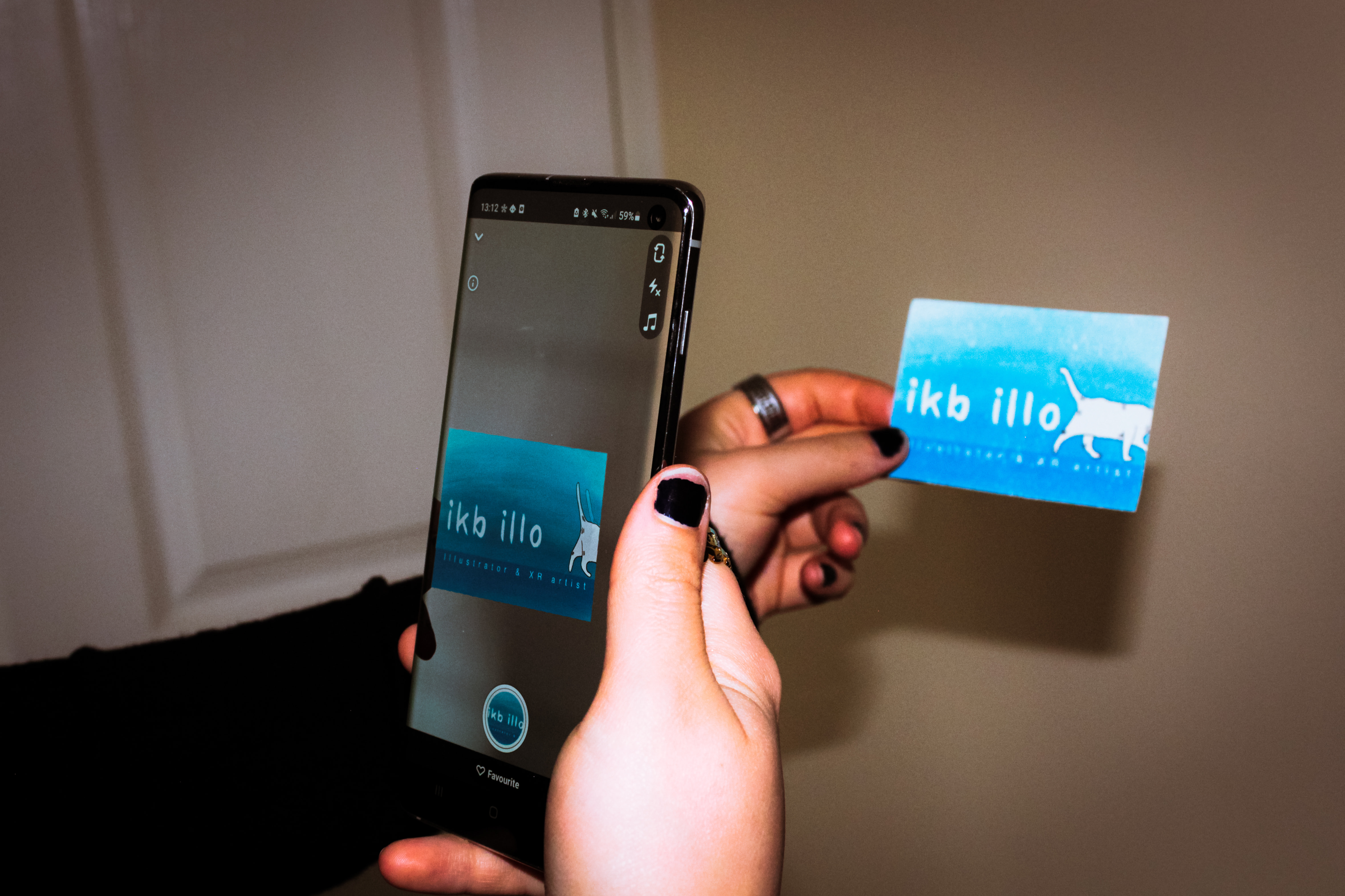 Photograph of a phone scanning the business card and showing an animation of a cat walking across the business card to reveal the words ikb illo.