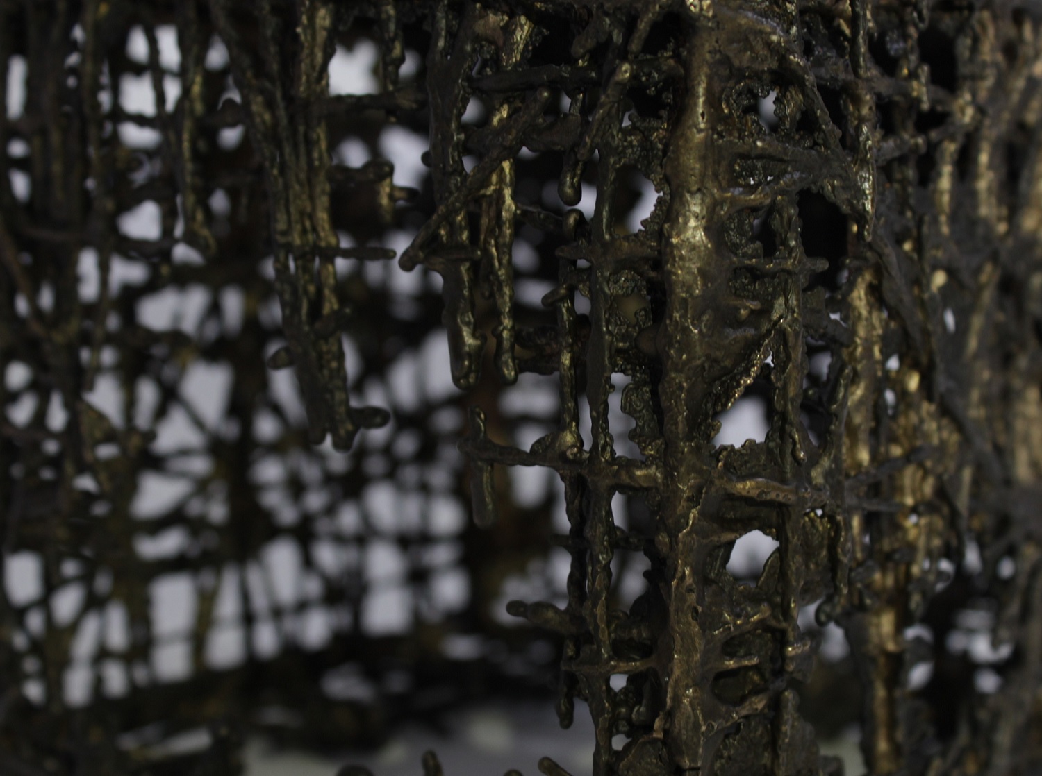 Sculpture by Jo Bellamy. Image of a detail of a larger work. Images shows a close up of a random mesh made of bronze. The whole piece (not visible) is a mesh cube, each side is 12.5cm. The casting process has failed to fully form the mesh which has gaps and there are holes in the structure