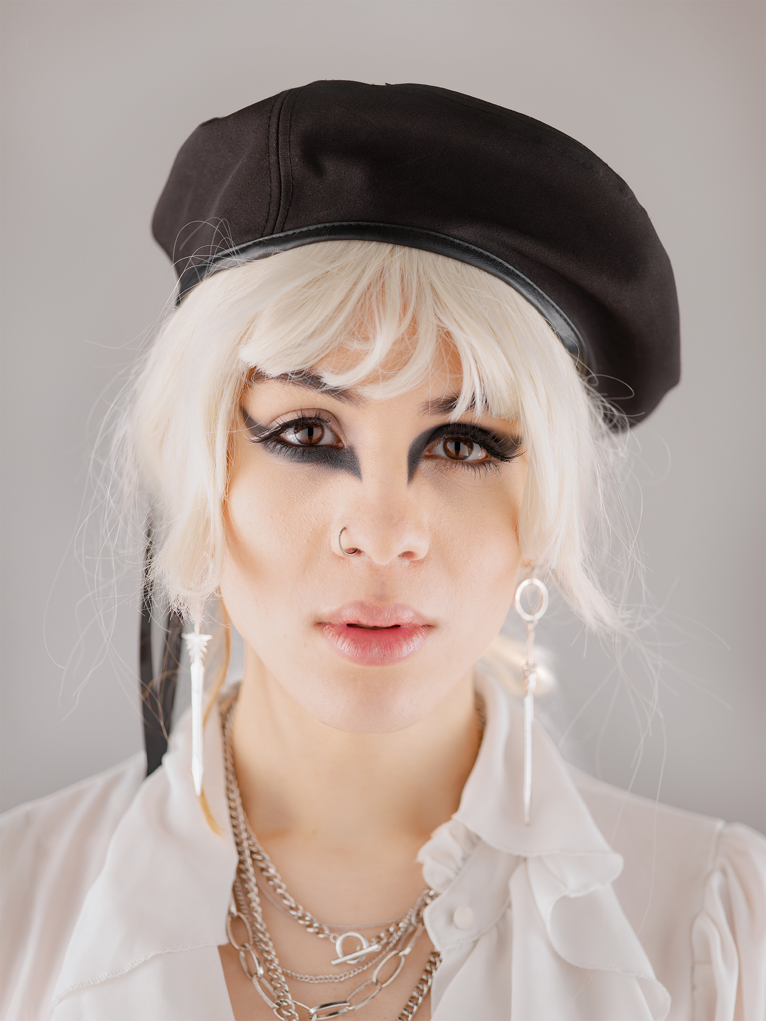 Subject is wearing a black beret, white wig and bold eyeliner, looking into the camera with a blank expression.