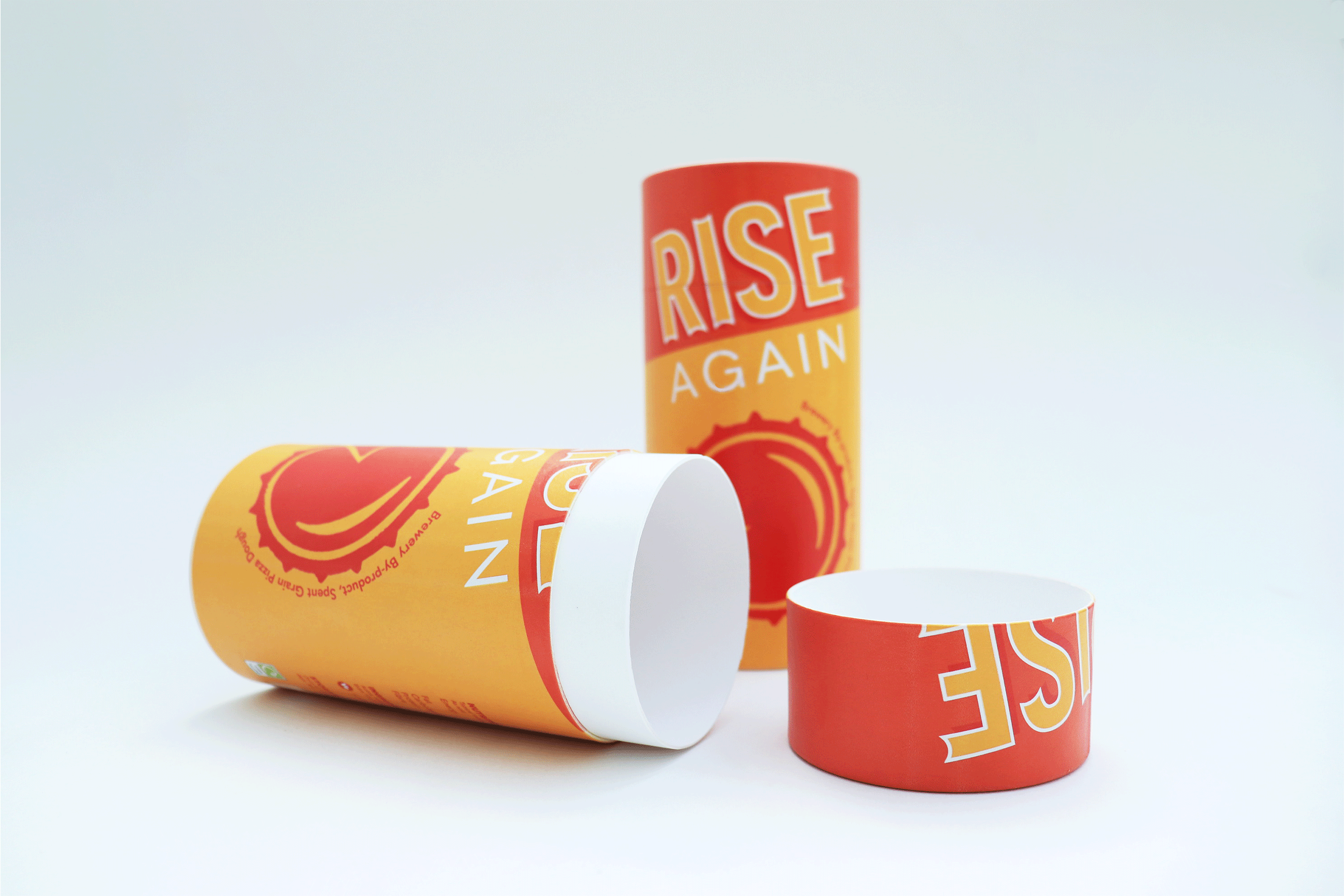 Graphic Design Packaging by Maika Elsley Medina, showing 2-cylinder packages in a bold red and yellow colour, featuring a upward sloping typeface spelling 'Rise Again' and a circular bottle cap design with a pizza like slice cut from it, displayed at the front.