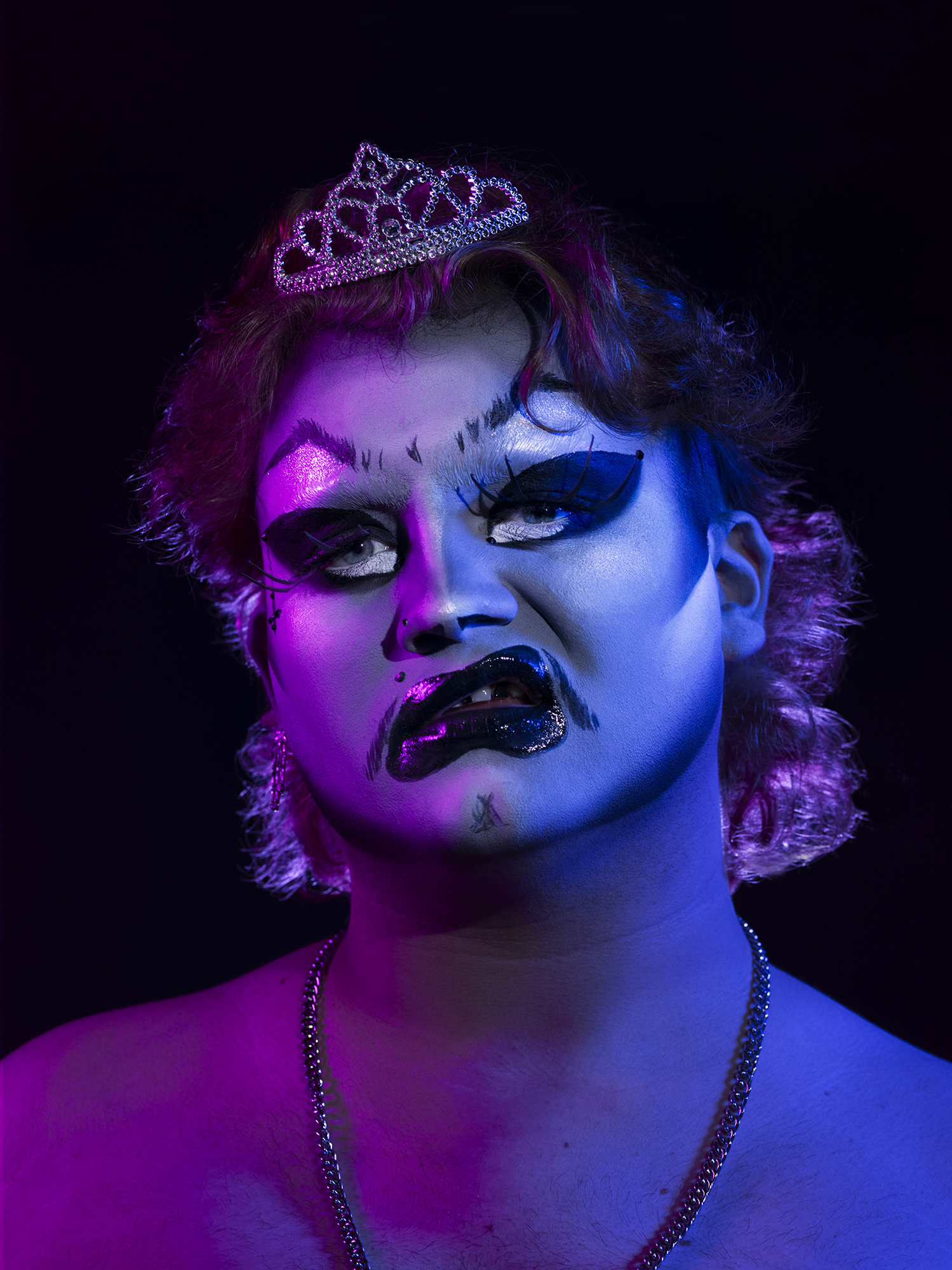 BA Photography work by Micha Hollis showing a portrait of drag artist Brat. The lighting is multi-coloured with pink on the left and blue on the right.