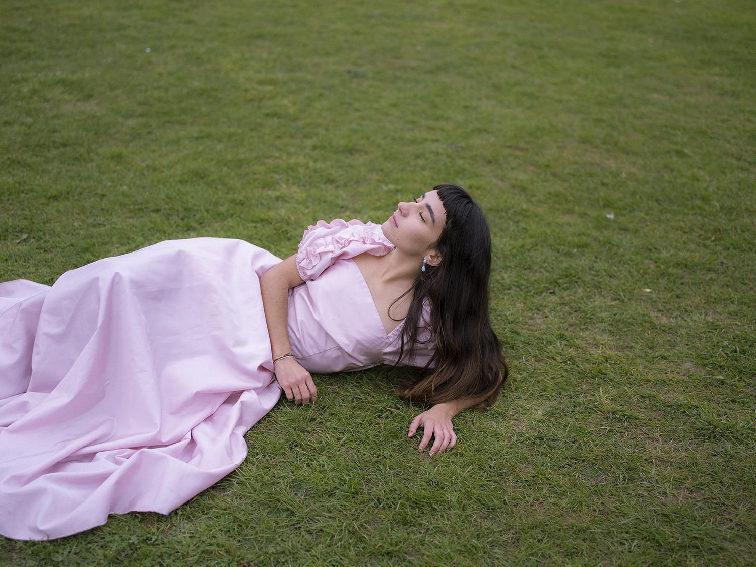 BA Photography work by Nicola Faye Bates showing a girl in a pink dress lying in a big grass field.