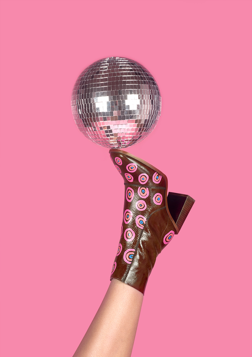 BA Photography work by Becca Stevenson showing a leg wearing a boot with a disco ball balanced on top, against a baby pink backdrop.