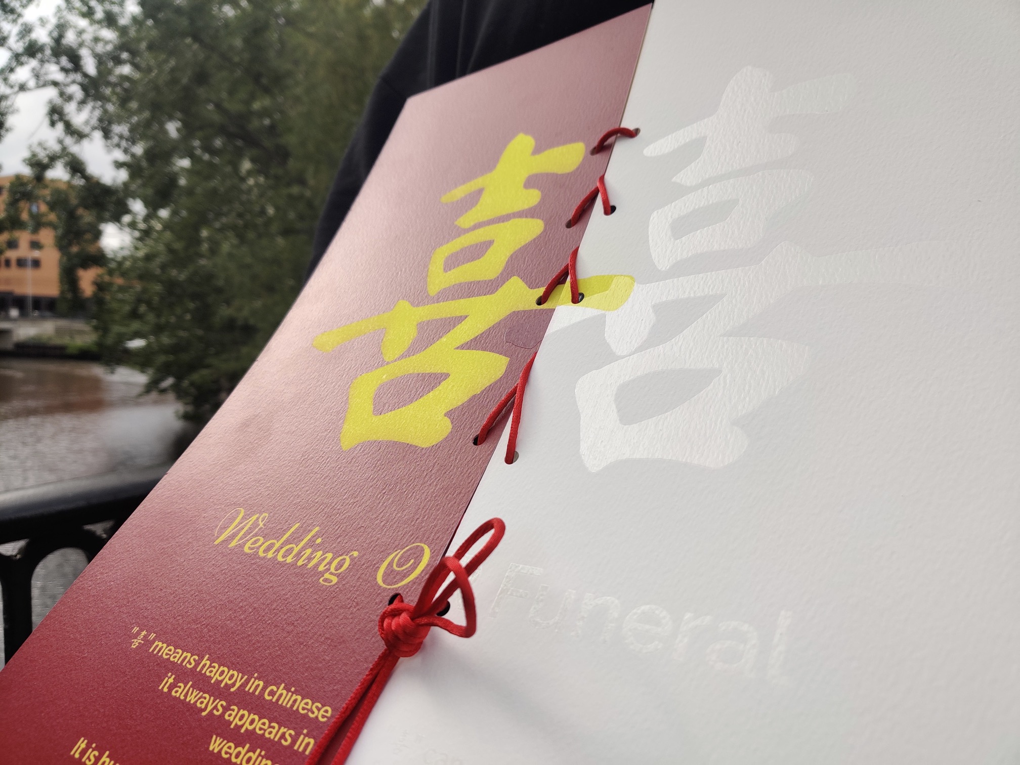 BA Graphic Communication work by Olivia Jia showing a ghost marriage campaign. A photograph of an invitation of two halves. On the left, it's coloured red with yellow writing announcing a wedding. On the right, the invitation is pure white, with a clear spot UV outlining the text, announcing a funeral