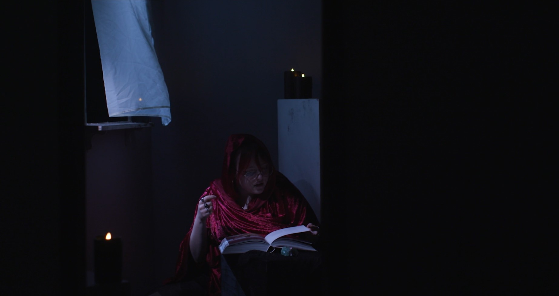 Image link to graduate showreel by Abi Plant showing a collection of short clips from our production design work. Image shows a character in a red robe reading a book in a dark room