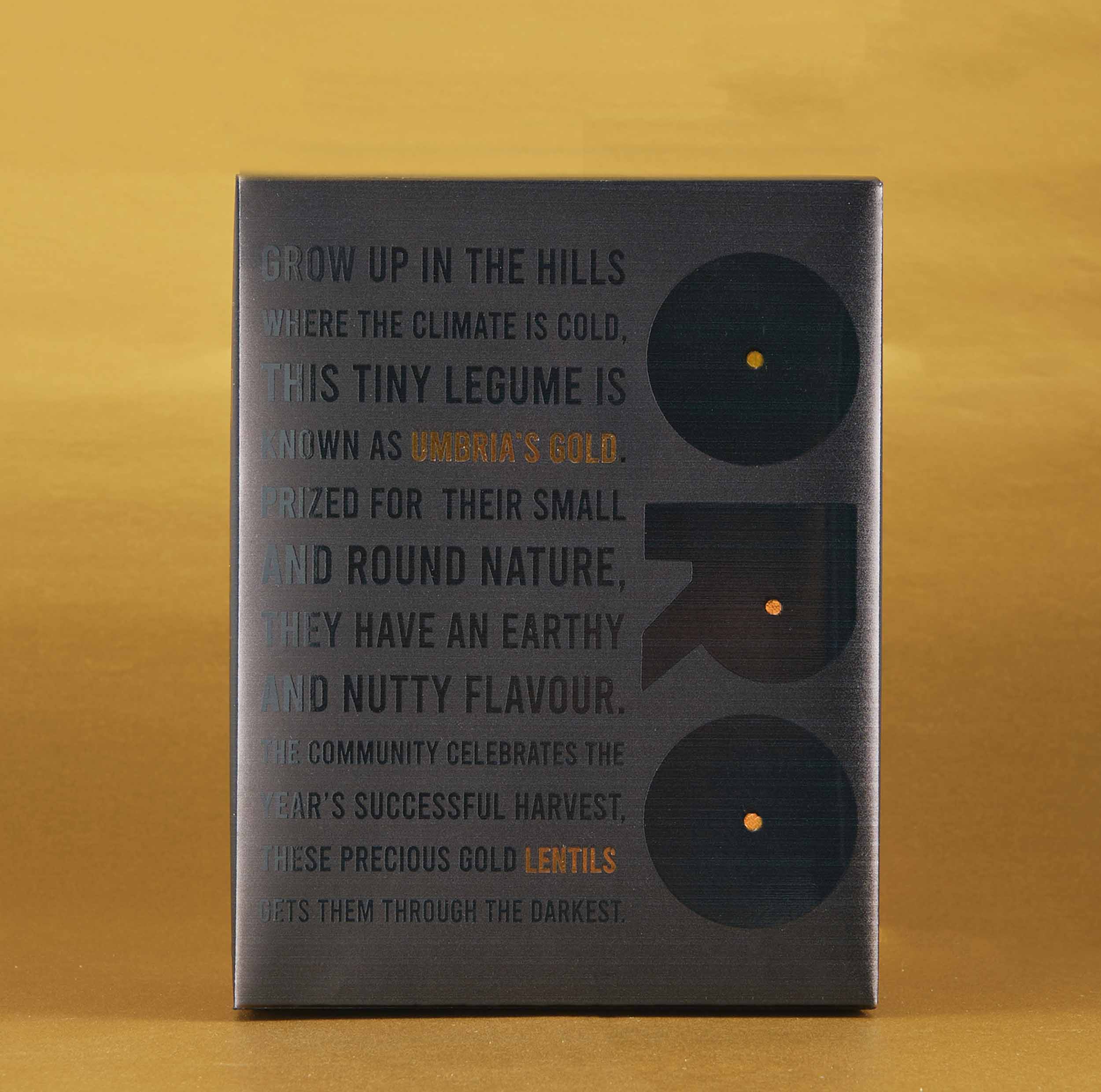 A photograph of premium lentil packaging sold to aid those effected by the earthquakes in Italy, black text on black packaging with orange text highlights.