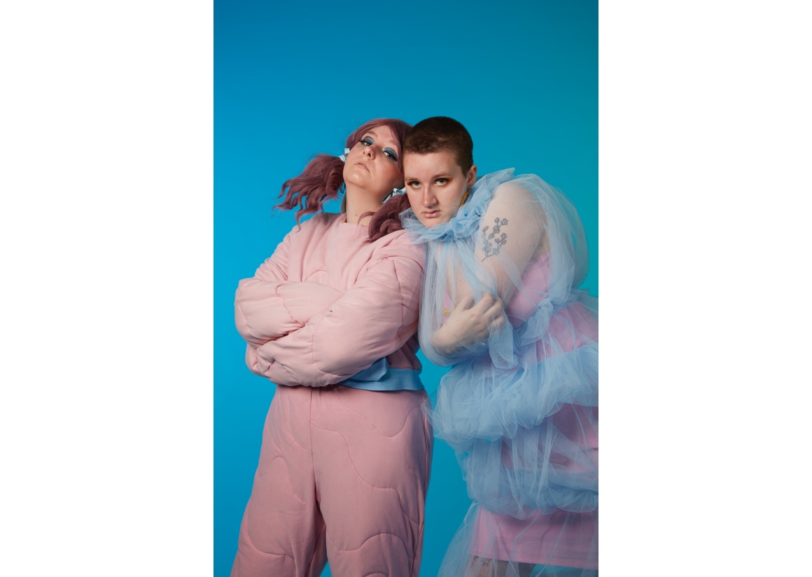 Models wearing Garment 1 and 2 by Bryan Griffiths (taken by Adam Billings) that is created from Tulle netting, hand dyed Jersey Fabric and elastic fabric bands and ribbing materials, photo against blue backdrop.