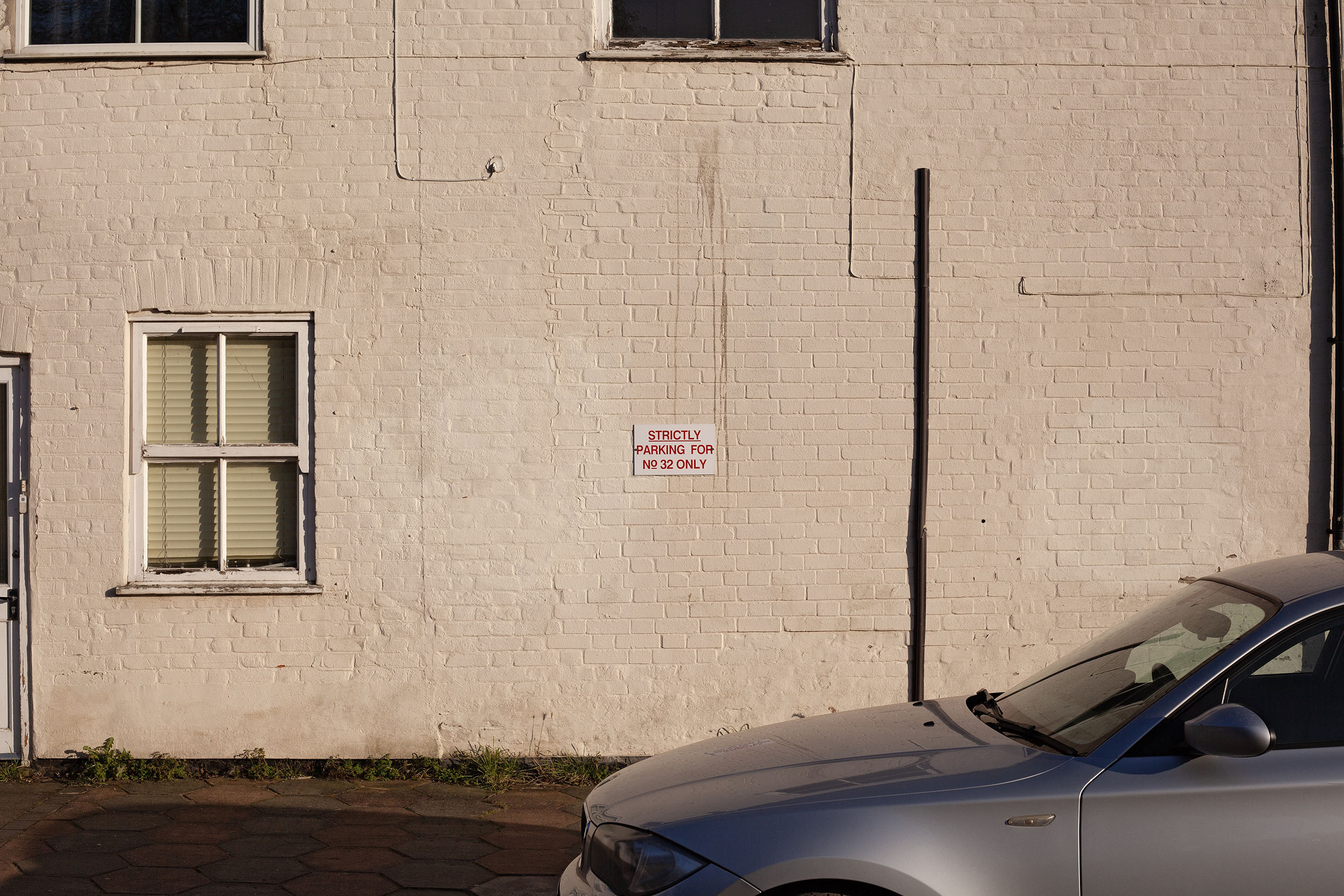 Photograph by Cerys Leahy depicting shadows and a car parked in-front of a strict parking sign.