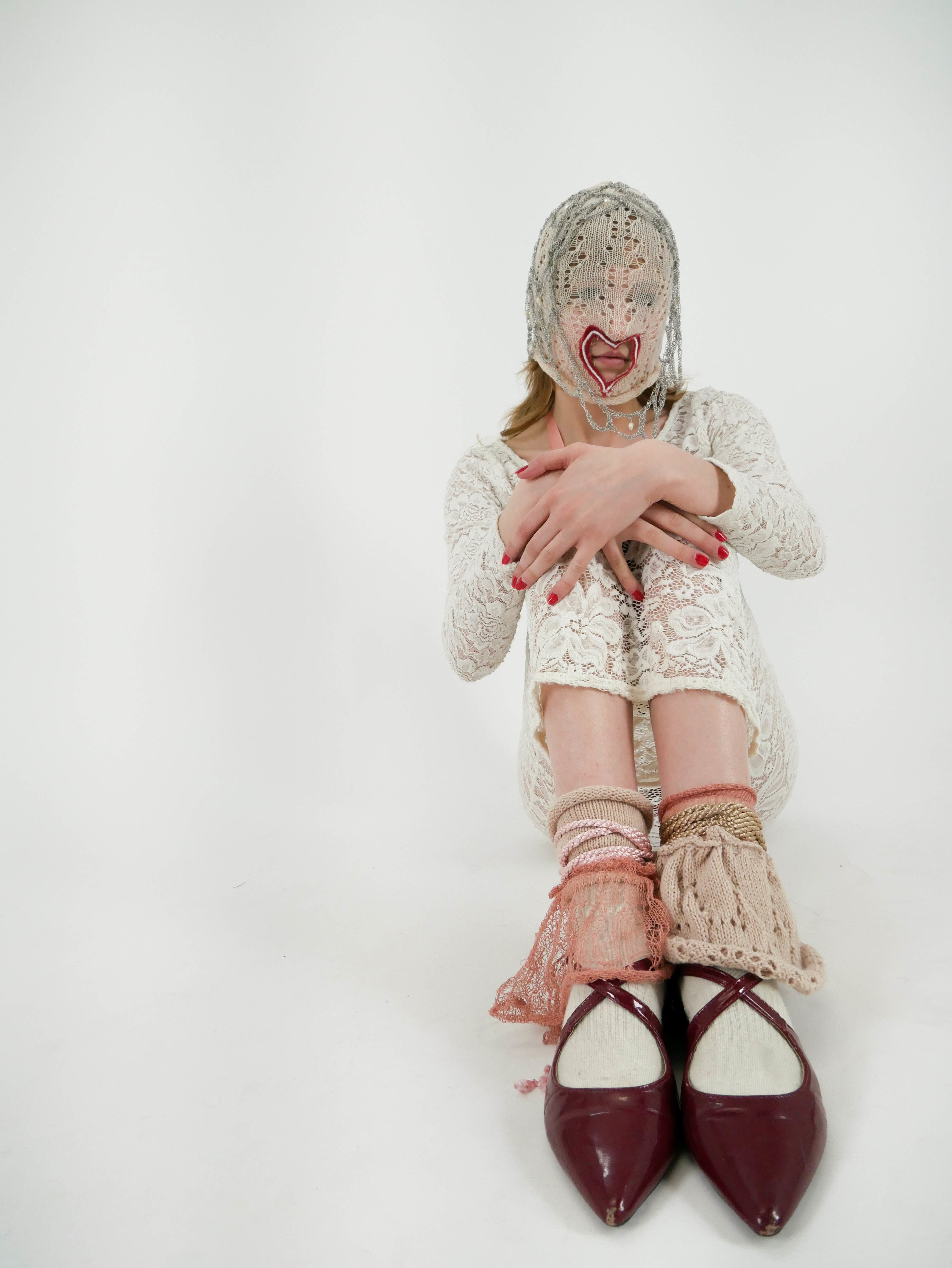 Model sat with knees to chest wearing knitted mask and legwarmers
