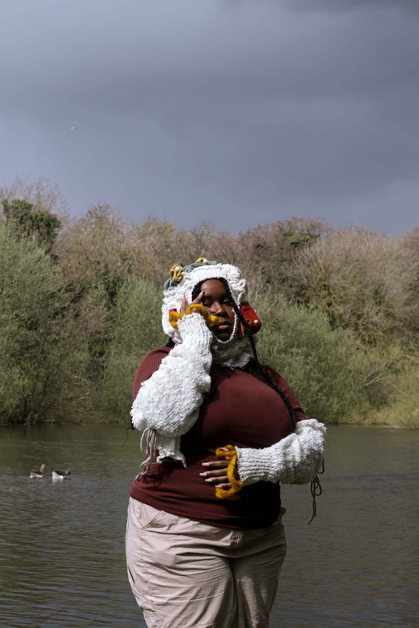 Model posed infront of a river and trees wearing pale knit headpiece and sleeves.