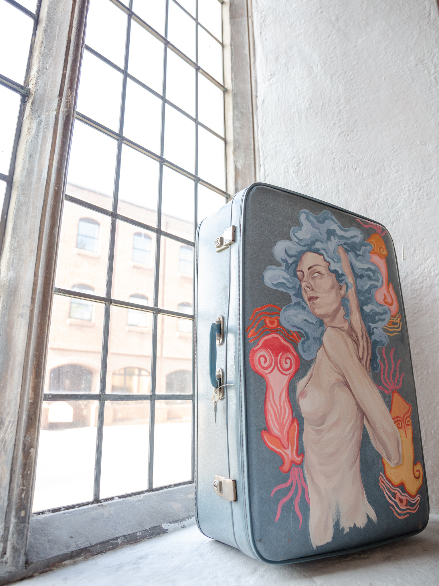 Fine art work by Elly Lynn, Acrylic painting on suitcase, showing imagery of the female form and creation symbology.