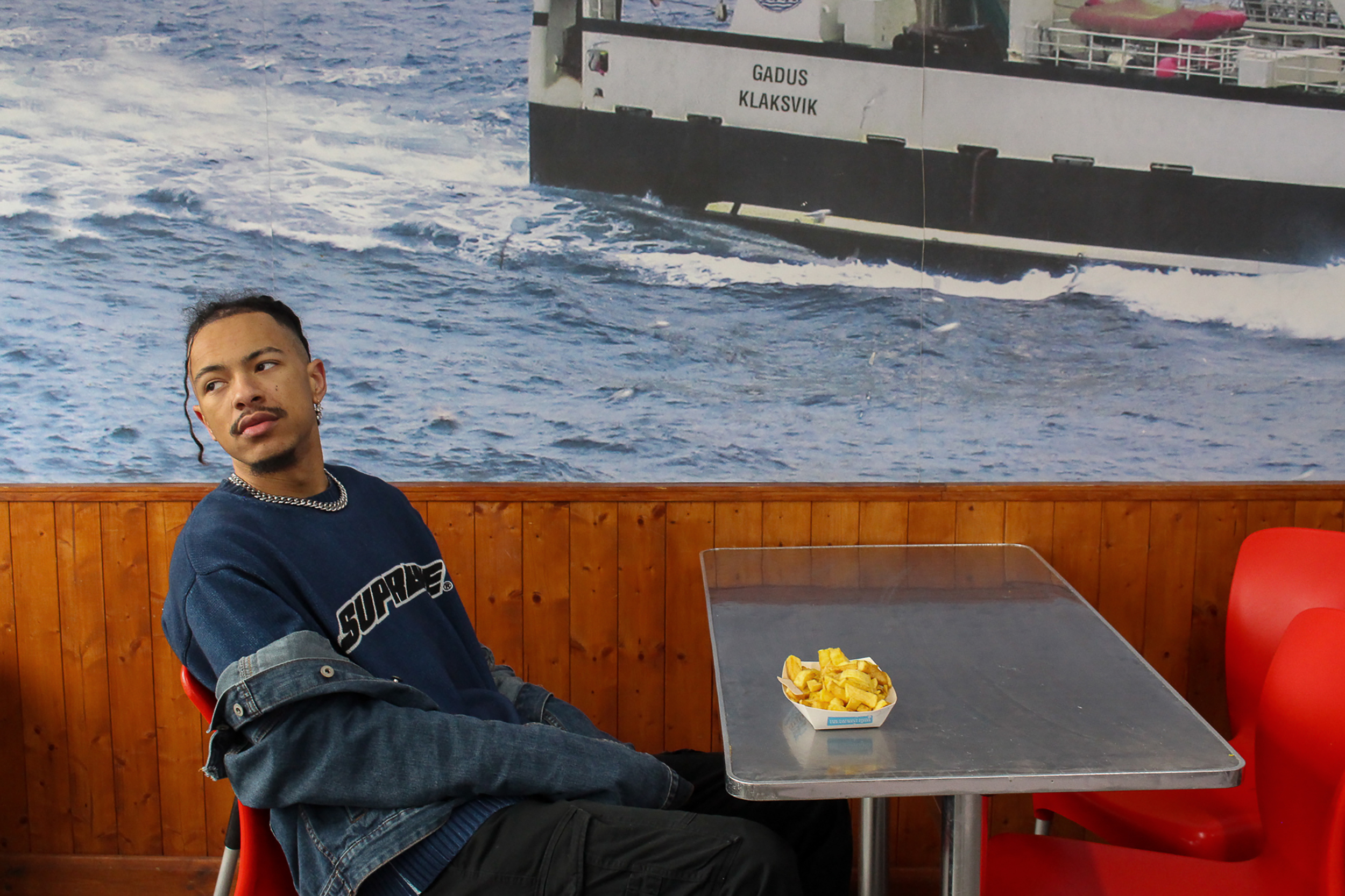 Photography, Styling and Direction by Ellie Parnham of model in fish and chip shop with some chips on the table.