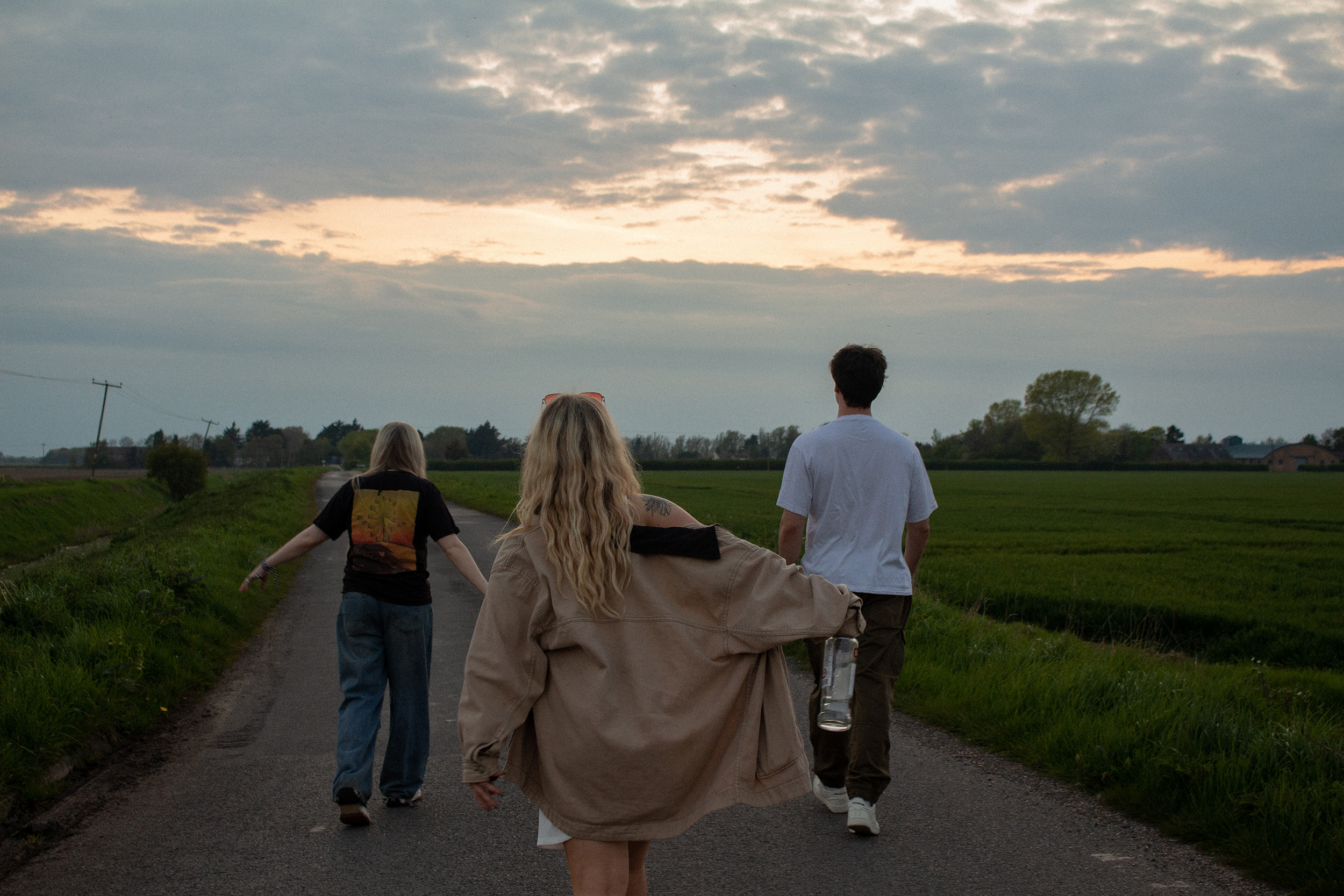 Photography, Styling and Direction by Ellie Parnham of three models walking away from camera on country road by fields.