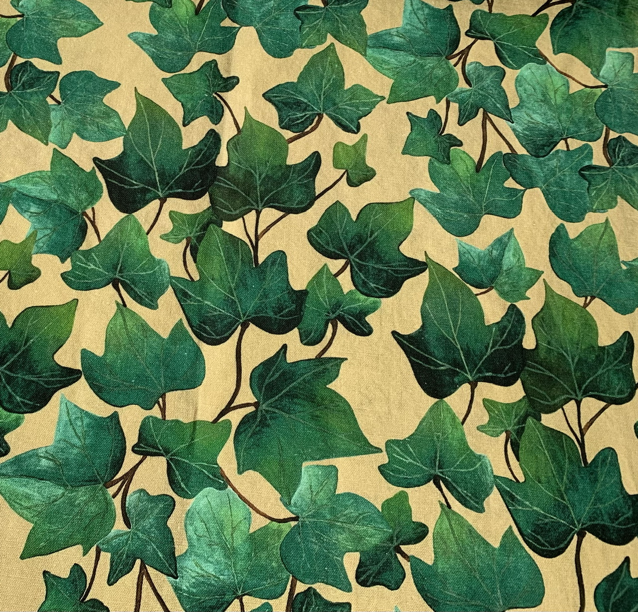 A repeat pattern design printed onto a cotton linen fabric, showing a light beige background with big ivy leaves vining up the fabric.