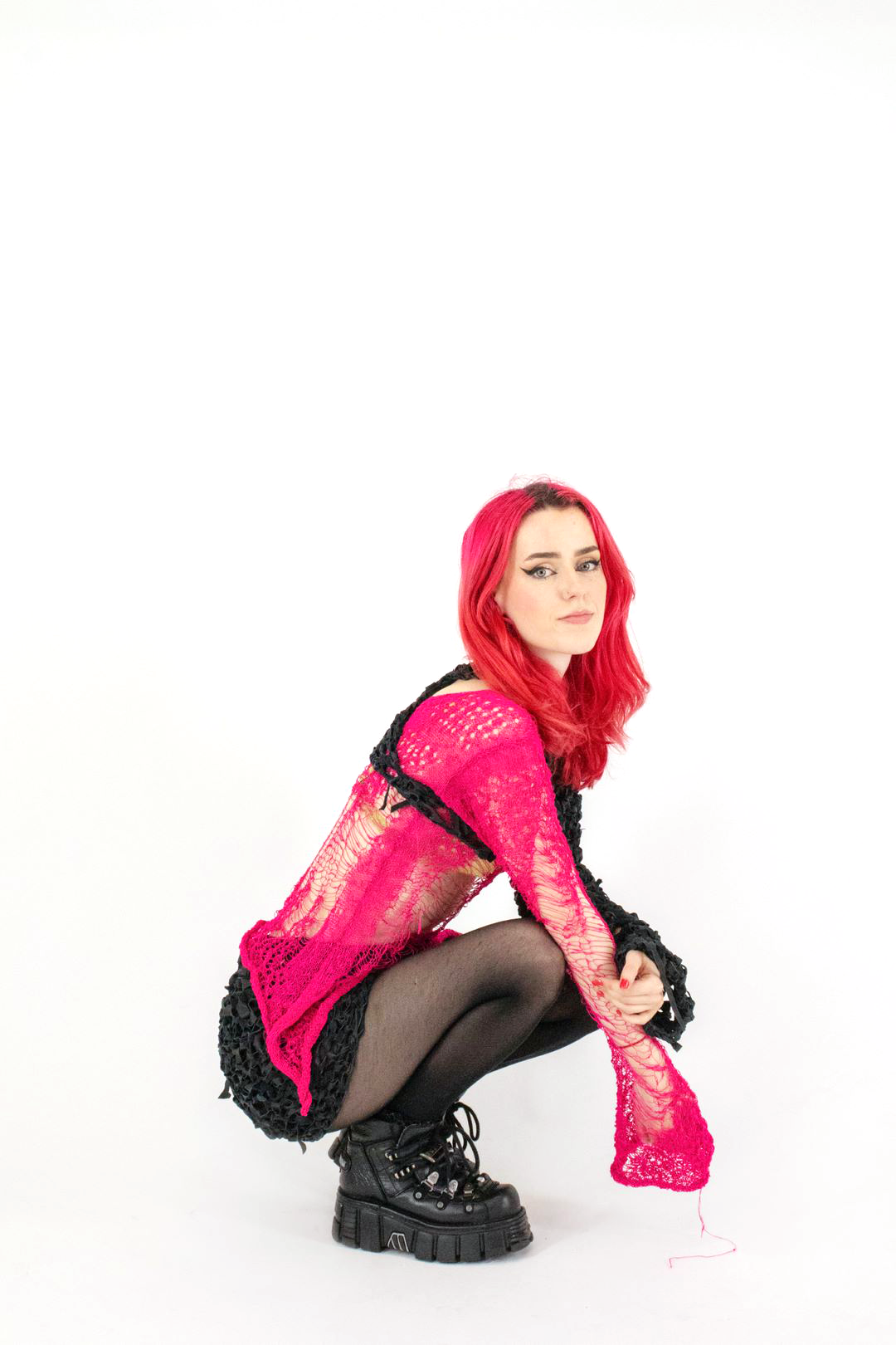 Model wearing Outfit 1 photographed by Ciara Roche. Outfit combination of knitted and crocheted pieces in hot pink and black with long sleeves and a skirt.