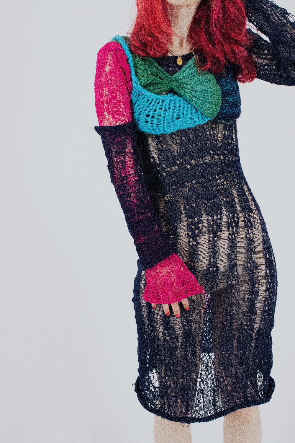 Model wearing Outfit 2 photographed by Ciara Roche is a combination of hand and machine knitted pieces. Main dress is black with long sleeves, one sleeve hot pink, layered pieces over the top part of dress in blue and green.