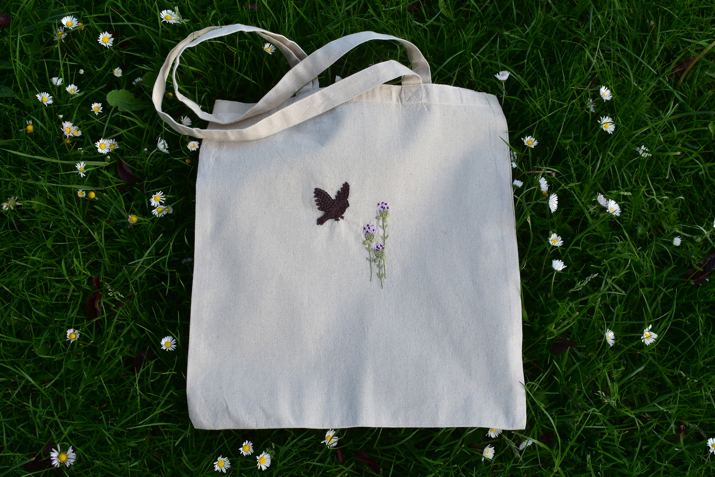 Hand-embroidered tote bag showing a silhouette of a goldfinch to the left of three common knapweed plants.