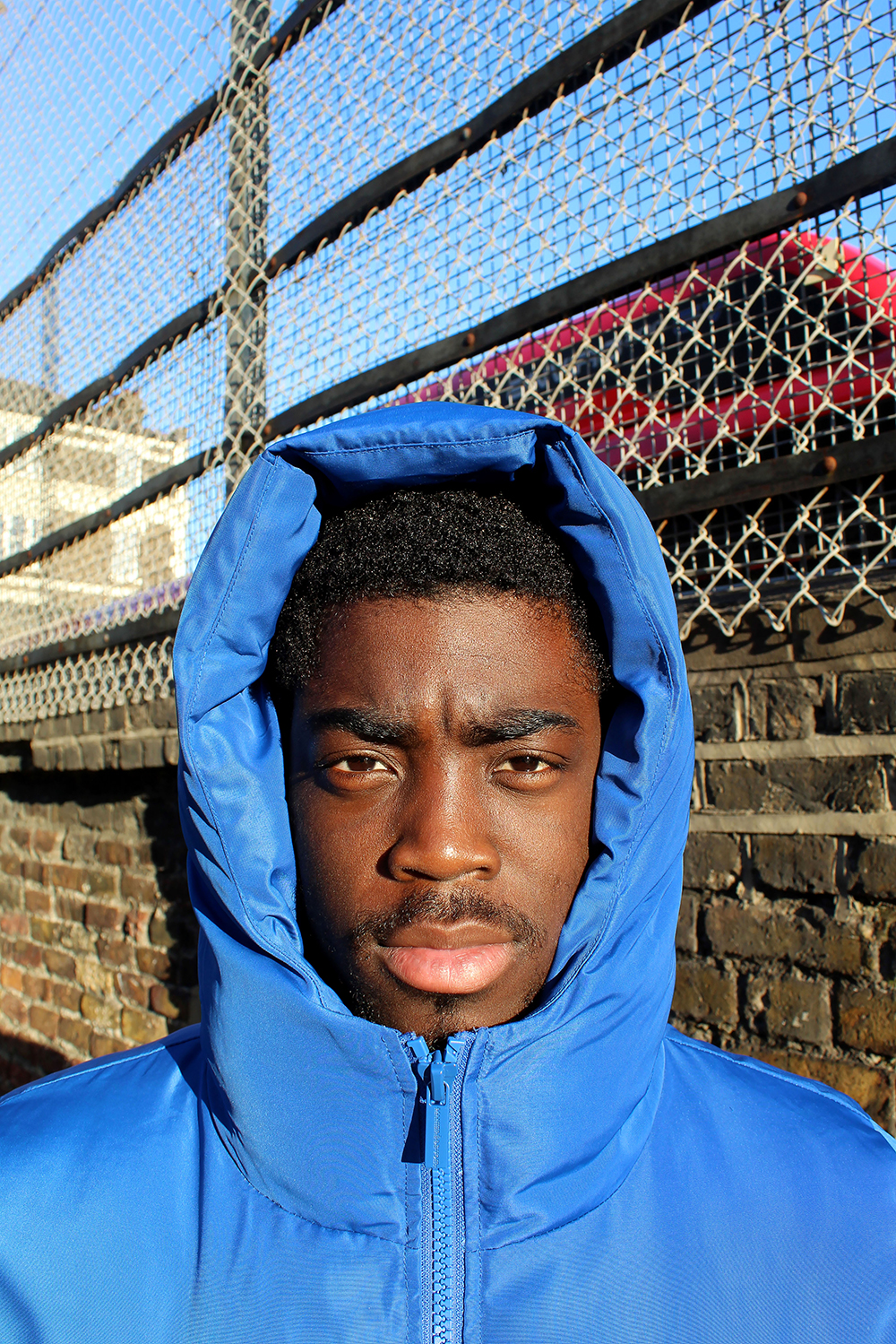 Fashion Portrait of model in blue jacket with hood up by Katie Healy exploring Sportswear In British Youth Culture