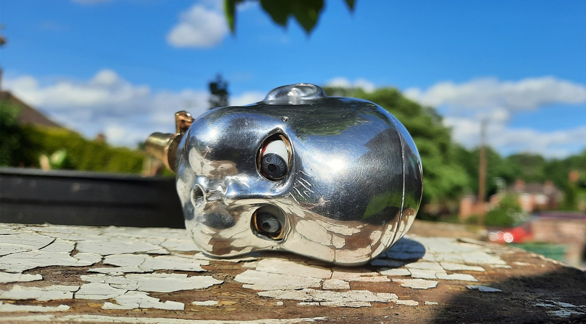 A metal Kinetic sculpture by Marek Jeczalik. A polished aluminium dolls head with glass eyes rests on its side in the sun (part of an automaton).