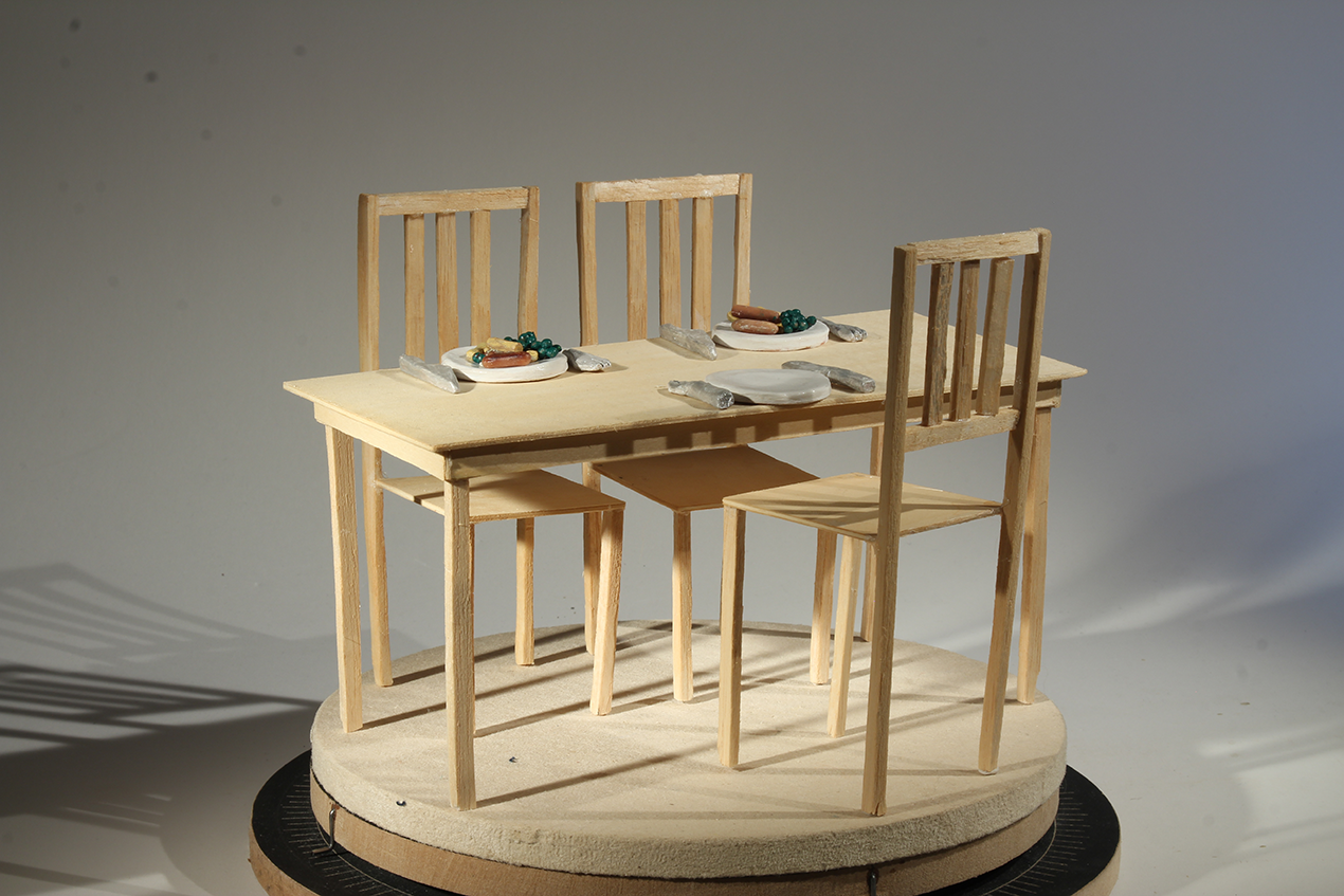 A picture of stop motion animation props. A table and 3 chairs with plates, food and cutlery placed on top.