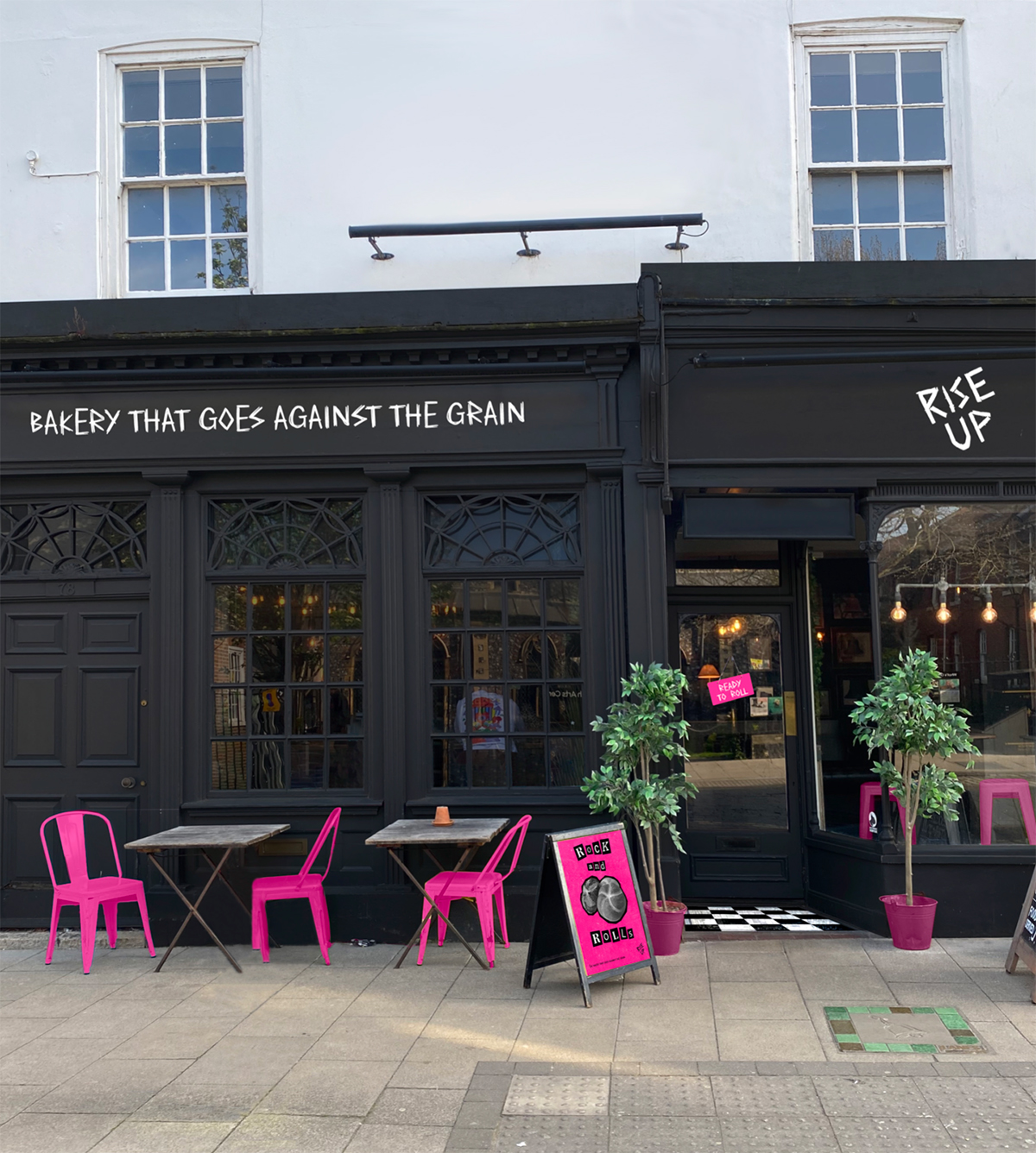 Rise up bakery exterior, painted black with white text and hot pink chairs outside.