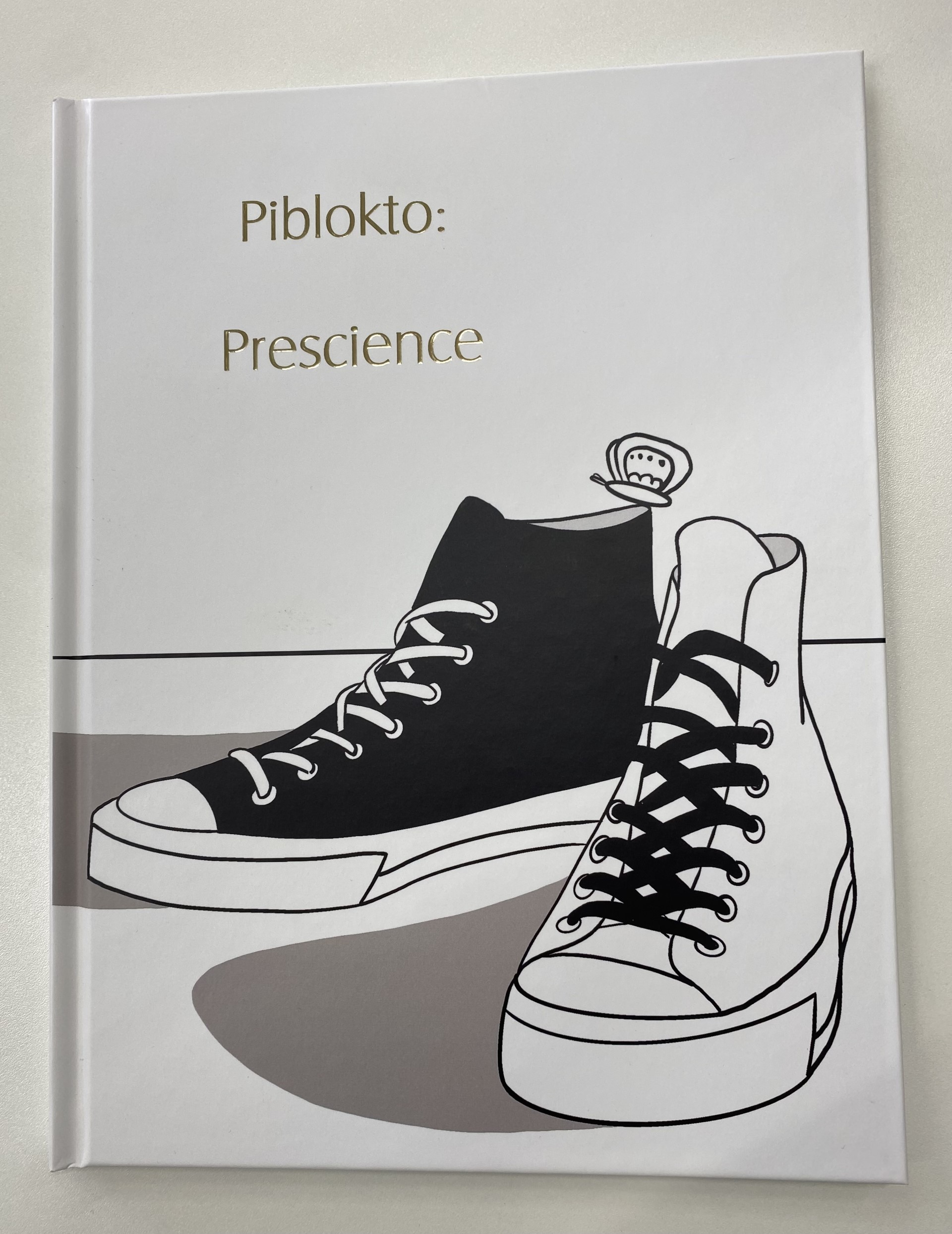 A picture of the cover of a Graphic Novel by Pui Ki Tse. The cover has two shoes, one black and one white, reminiscent of Converse shoes over a white background with a dark coloured text on the top left corner "Piblokto: Prescience".