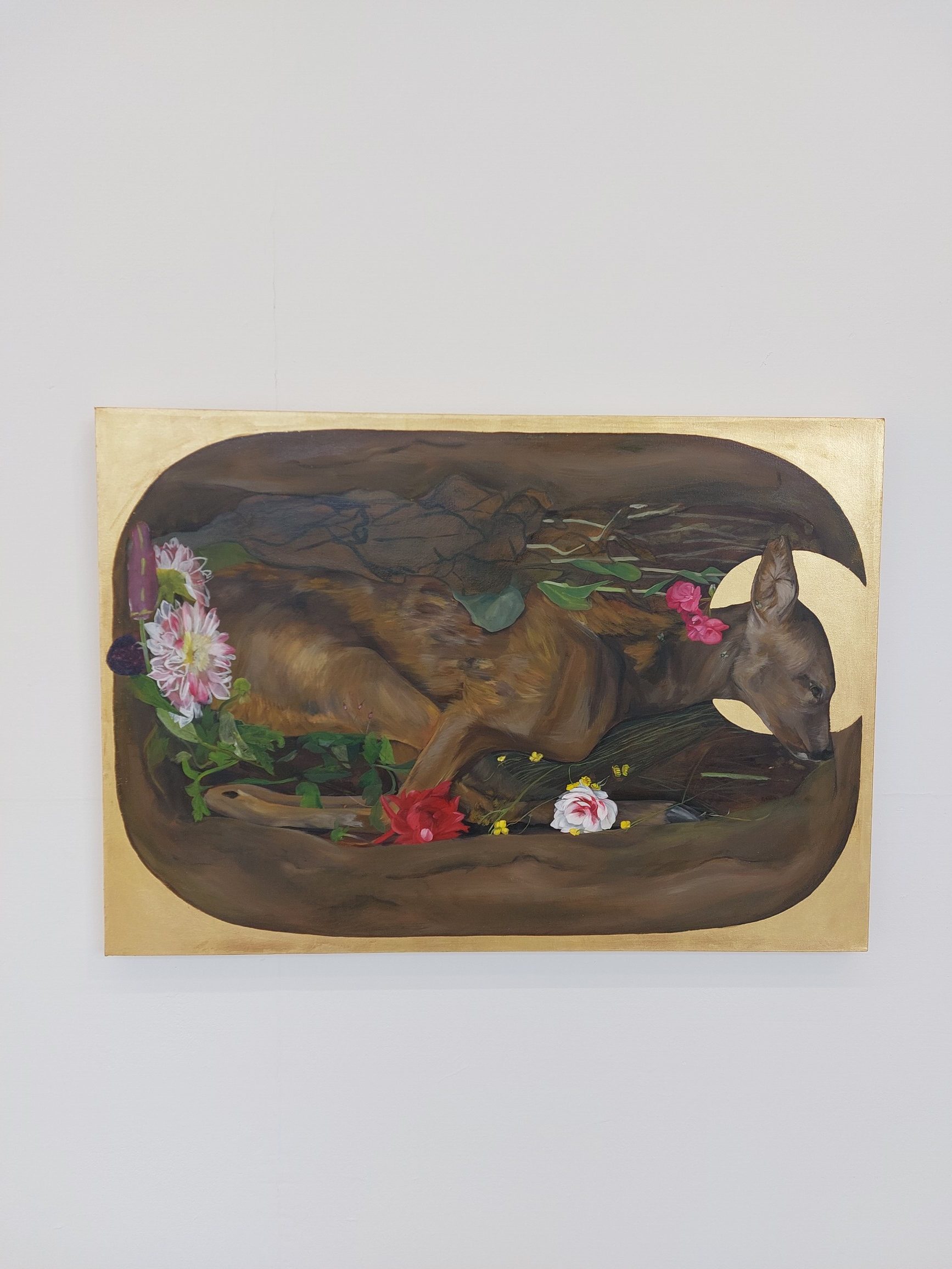 Oil painting of a deer curled into a resting pose in a grave from above surrounded by flowers and plants, encircled by gold with a gold halo around its head.