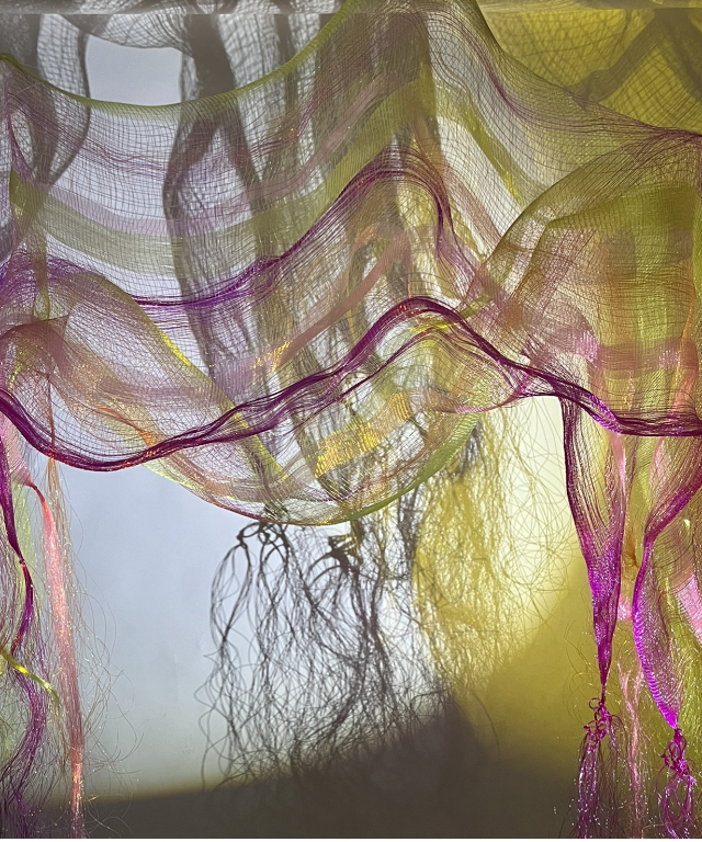 Image of hanging woven fabrics in yellows and pinks and the abstract shadow they create.