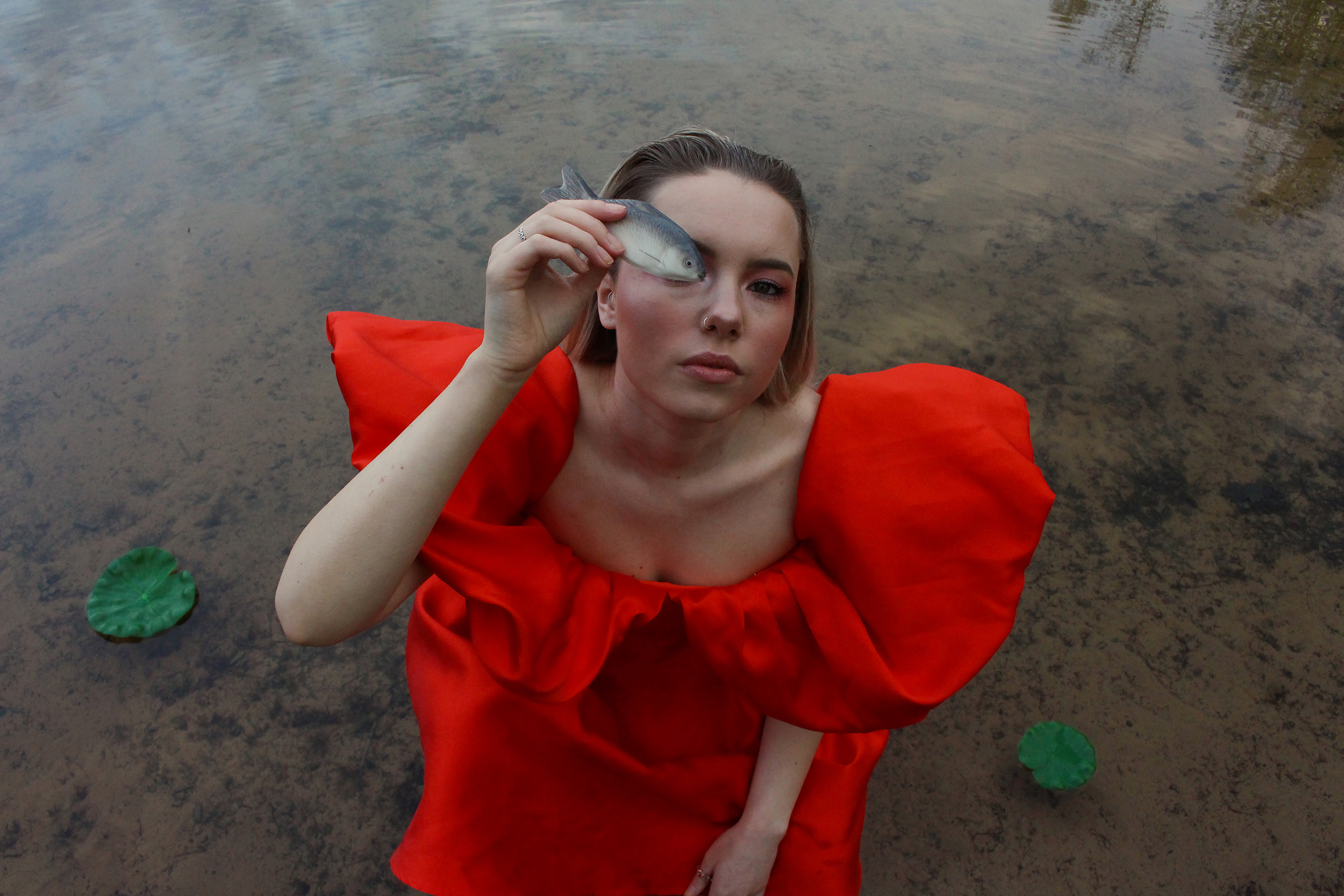 Picture of model in red dress holding a toy fish up to their eye. Creative Direction, Photography and Styling by Rosie Parnham.
