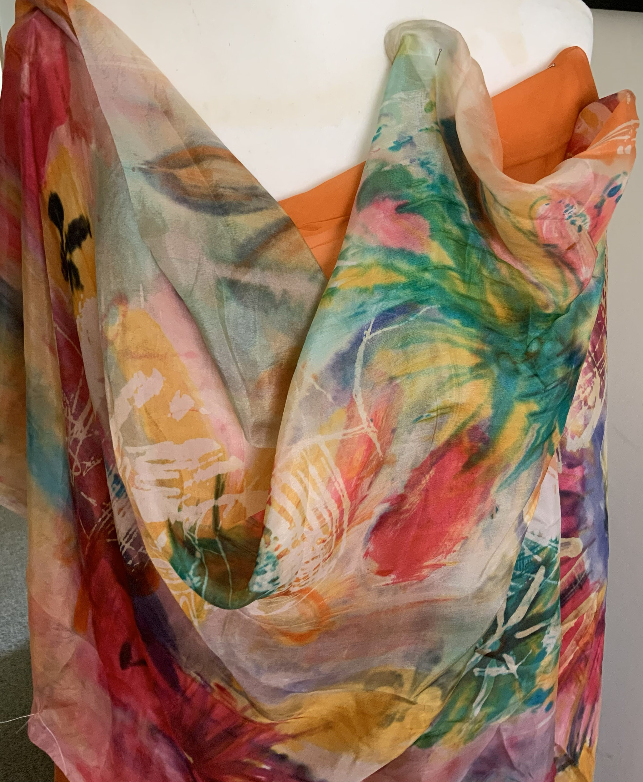 Hand-painted floral patterned silk scarf with reds greens and yellows draped over a mannequin