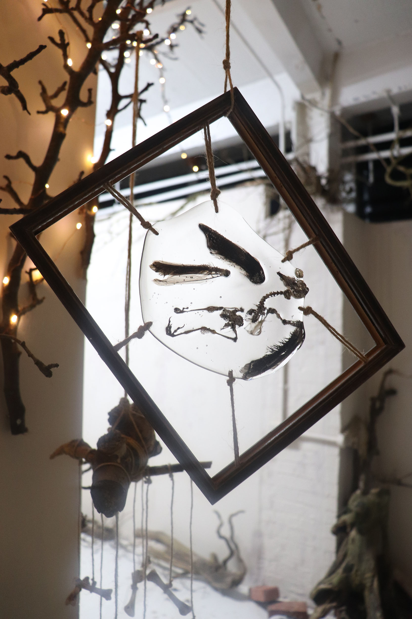 Free hanging artwork by Zoë Bullen, displaying skeletal remains with some feathers, of a cat caught robin, arranged in resin, and suspended within an old wooden picture frame.